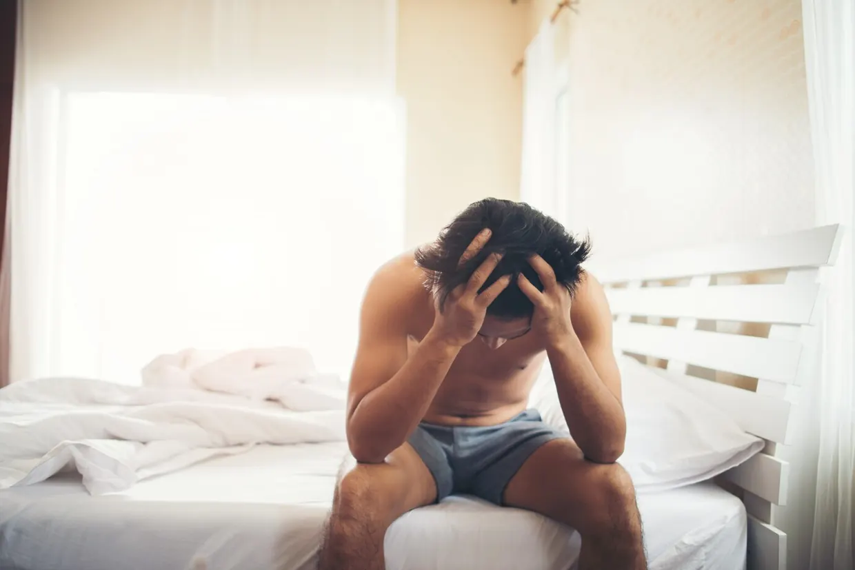 A tired man sitting on the edge of his bed